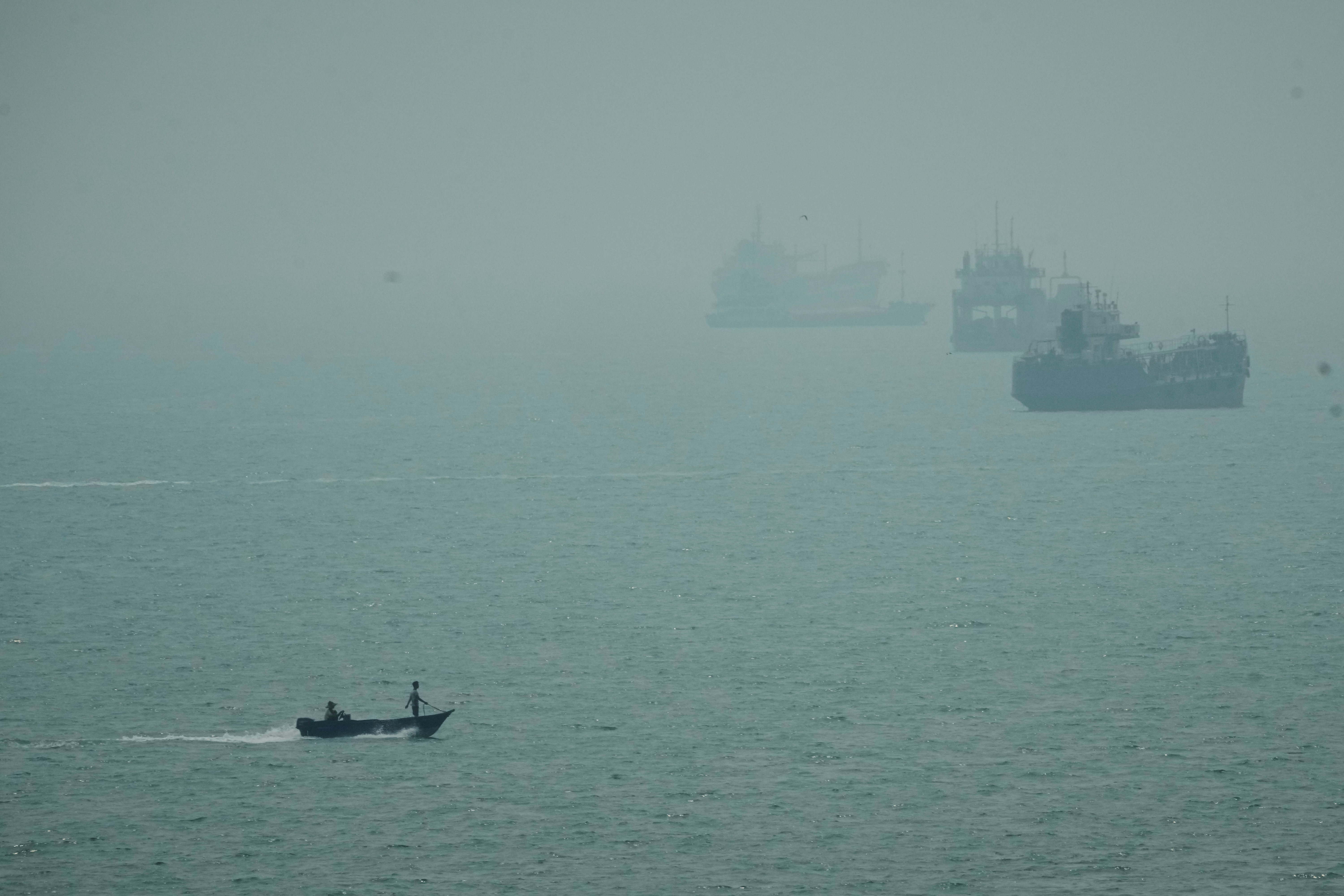 A motorboat travels past commercial vessels anchored amid haze in the Strait of Hormuz off Bandar Abbas, Iran, Monday, Sept. 7, 2026.